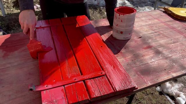 A houseworker repaints the shutters with red color.The alpine hut is being renovated. The man works with a brush and red paint.