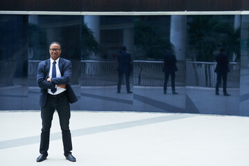 Obraz premium Full-length portrait of positive confident entrepreneur standing outdoors, crossing arms and looking at camera