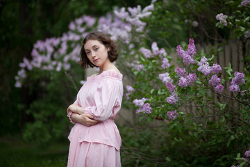 beautiful young girl, a brunette in a pink dress walks in the lilac garden, a peasant woman in the village