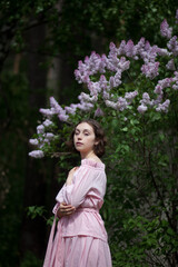 beautiful young girl, a brunette in a pink dress walks in the lilac garden, a peasant woman in the...