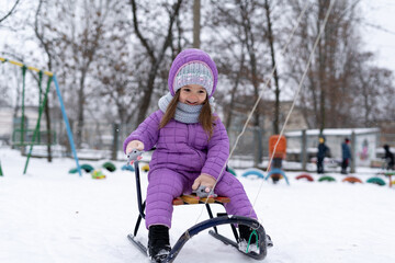 Fototapeta na wymiar Portrait of a happy girl. A child in winter is dressed in a purple bright jacket to go sledding during the summer holidays.