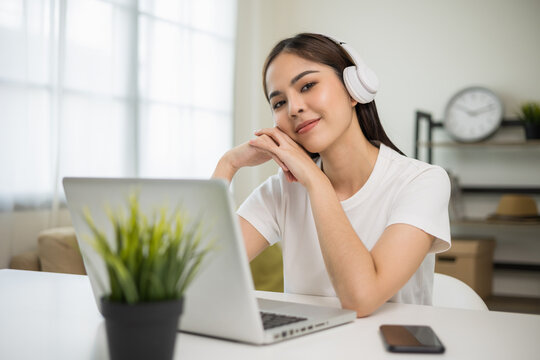Young asian woman in headphone using laptop chatting video conference online sitting in living room at home. Business Woman look at screen Meeting on social live steam. Work, learning from home.