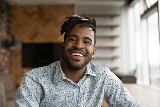 African stylish hipster guy with dreadlocks hairstyle wide toothy smile sit indoor look at camera. Video call event profile picture, portrait of successful entrepreneur pose in modern office concept