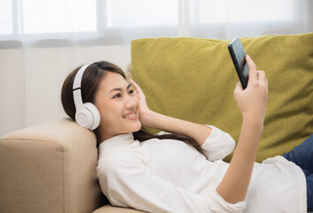 Relaxing time on sofa. Beautiful young asian woman lay down on sofa and listening to the music with headphone. She has rhythm Lifestyle in living room at house in the morning.