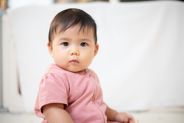 Fototapeta premium An Asian girl about 1 year old. Playing in the living room in the house. A cute baby wearing a pink dress Stay with parents in the house
