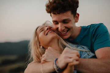 Young couple on a walk in nature at sunset in countryside, hugging and having fun.