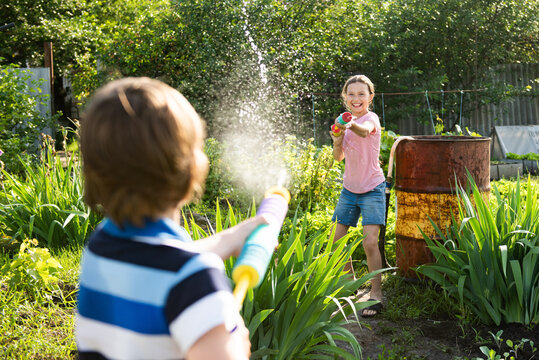Cheerful girl and boy shooting water pistols in the backyard