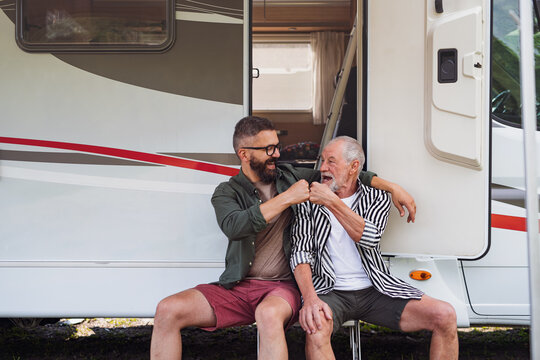 Mature man with senior father sitting by car outdoors, fun on caravan holiday trip.