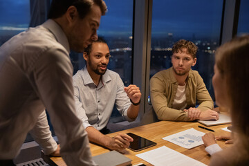 Group of multi ethnic colleagues businesspeople gathered together in boardroom discuss collaborative project work until late in modern office. Briefing activity, workshop, deadline, workflow concept