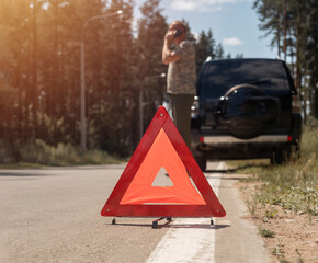 Triangle caution sign on road after car break and driver speaking on mobile phone, calling for...