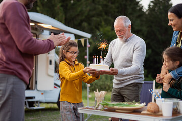 Multi-generation family celebrating birthday outdoors at campsite, caravan holiday trip.