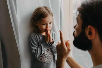The father puts the child in a corner and makes remarks for bad behavior by waving his index finger near his face. The child does not want punishment and apologizes - obrazy, fototapety, plakaty