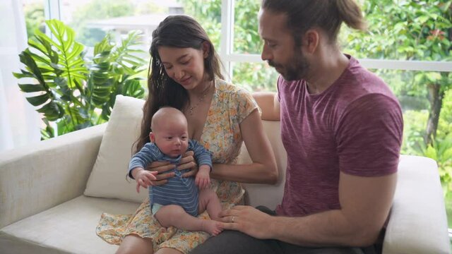 Happy Family relaxing at home. Caucasian parent mother and father sit on sofa caring sleeping adorable newborn baby infant son together in living room. Family relationship and baby healthcare concept.