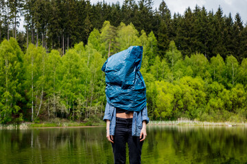 woman with plastic bag on a head stay next to lake in autumn time