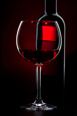 Red wine glass and bottle on red black background