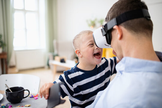 Father with happy down syndrome son indoors at home, using vr goggles.