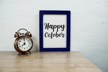 Happy October typography text and alarm clock on wooden table and white wall background
