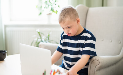 Down syndrome boy indoors at home, using laptop.