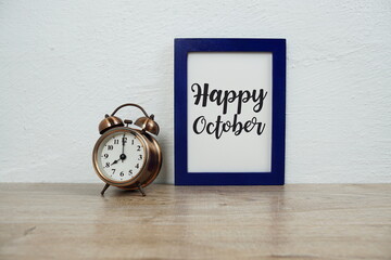 Happy October typography text with alarm clock on wooden table and white wall background