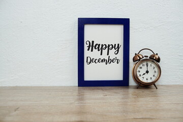Happy December typography text with alarm clock on wooden table and white wall background
