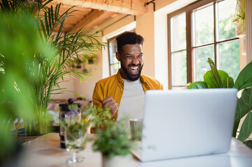 Cheerful young man with laptop working indoors, home office concept.