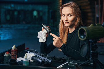 Professional female shooter cleaning her disassembled firearm - obrazy, fototapety, plakaty