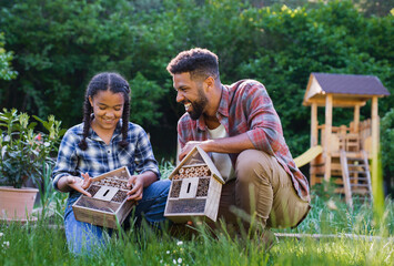 Happy young man with small sister holding bug hotels outdoors in backyard, laughing.