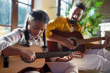 Happy father with small daughter indoors at home, playing guitar.