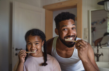 Happy young father with small daughter brushing teeth indoors at home, sustainable lifestyle.