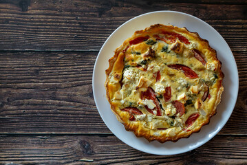 Delicious homemade quiche with feta cheese, tomato, spinach and onion. Homemade puff pastry quiche on the parchment paper. Weathered plank barn wood background top view. Copy space.
