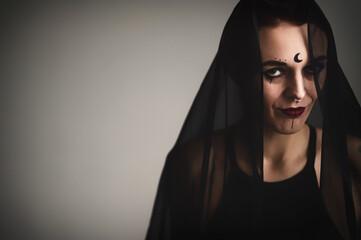 Redhead woman with a black veil on her head in a dark studio. A girl with an earring in her nose smiles slyly. Witch Makeup. Halloween costume.