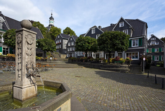 Town square at Solingen-Gr&auml;frath with fountain and slate-covered buildings, church on the hill in background