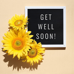 Get well soon, text on letter board with sunflowers. Flat lay with natural flowers and motivation message on black letterboard on beige natural paper. Sunshine with long shadows.