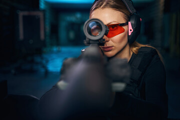 Serious woman using a telescopic sight mounted on the weapon - obrazy, fototapety, plakaty