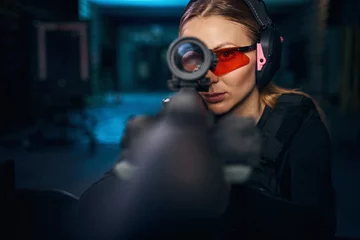 Tuinposter Serious woman using a telescopic sight mounted on the weapon © Svitlana