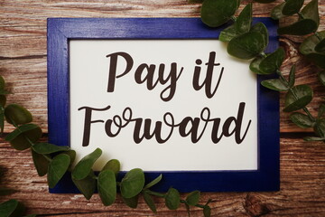 Pay it Forward written on blue frame with green leave flat lay on wooden background
