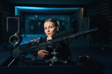 Serious cute shooter with her firearm sitting at the table