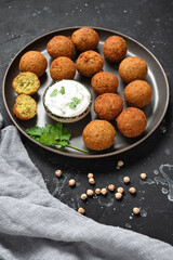 Falafel balls with yogurt sauce in a plate on a black stone background. Top side view, selective focus.