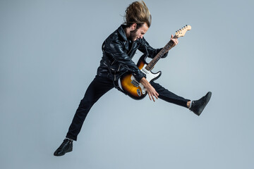 emotional bearded rock musician playing electric guitar in leather jacket and jumping, guitar player - obrazy, fototapety, plakaty