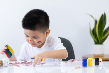 Smart little Asian boy having an idea while with painted hands at home. Learning and education of kid