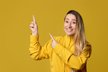 young woman pointing away on yellow background