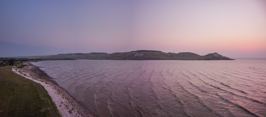 Panoramic landscape, colorful purple sunrise at coastline of Volga river in front of hills and cliffs. Waves on the surface of the water. Samara region, Zhigulevskoe reservoir, Russia 