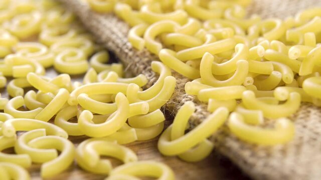 Uncooked Italian gobbetti pasta on rustic rough burlap and wooden surface. Macro. Dry macaroni. Dolly shot. Mediterranean cuisine concept