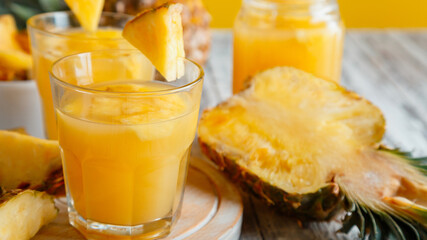 Tasty pineapple juice in glass with pineapple fruit slices. Fresh natural pineapple cocktail and juice in glass on white wooden table. Long web banner.