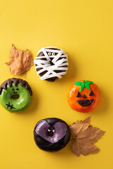Assortment of Halloween donuts and autumn leaves on yellow background