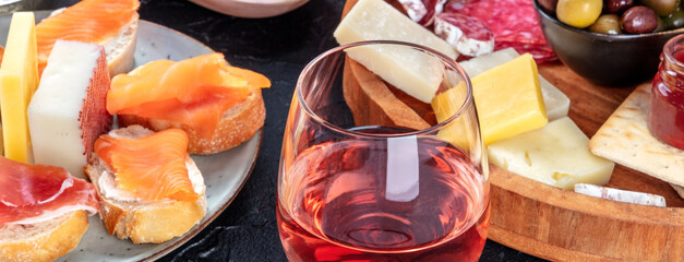 Rose wine with cheese, salmon sandwiches and olives panorama. Italian antipasti or Spanish tapas...