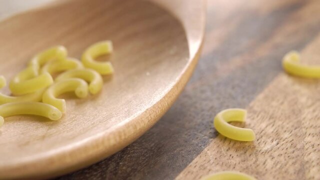 Raw dry traditional gobbetti pasta fall into a wooden spoon on a rustic wood board. European Italian food concept. Slow motion. Macro shot