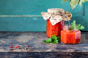 Homemade tomato ketchup made from ripe red tomatoes in glass jars with ingredients on an old wooden table. Copy space