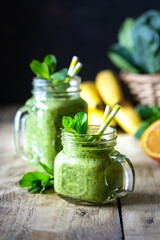 Two healthy green smoothies with spinach, banana, orange and mint in glass jar and ingredients. Detox, diet, healthy, vegetarian food concept.