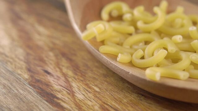 Falling dry uncooked italian gobbetti pasta on a kitchen wooden spoon on a wood table in slow motion. Macro. Traditional Italian Mediterranean cuisine. Raw macaroni